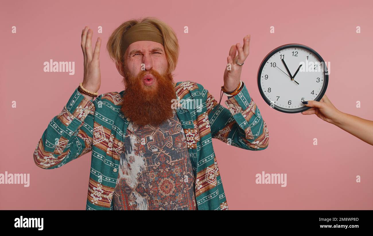 Un jeune hippie confus avec l'anxiété de vérifier l'heure sur l'horloge, courir tard au travail, étant en retard, échéance sur fond rose studio. Un homme sérieux qui regarde des heures et des minutes s'inquiétant d'être ponctuel Banque D'Images