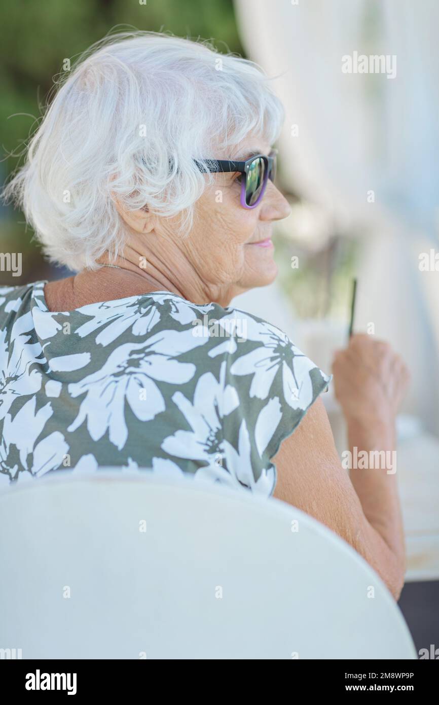 Belle femme sénior assise dans un café extérieur d'été Banque D'Images