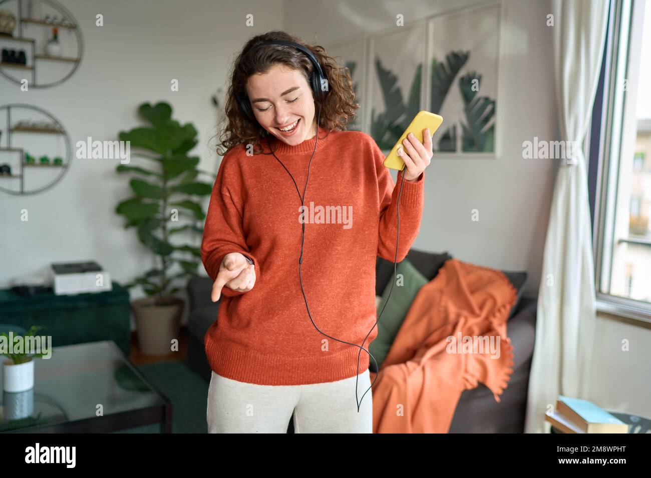 Bonne jeune femme dans un casque qui écoute de la musique mobile dansant à la maison. Banque D'Images