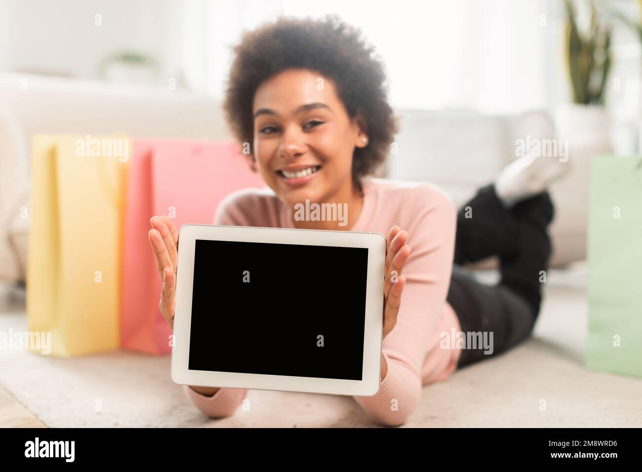 Souriant jeune mixte race femelle shopaholic mode blogger show tablette avec écran vide, se trouve sur le sol Banque D'Images