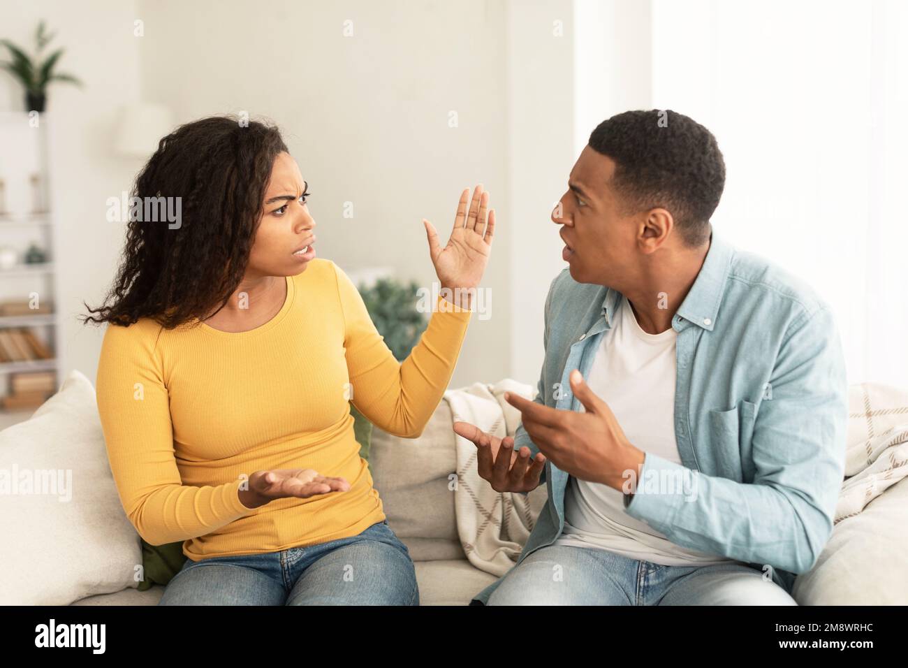 Jeune femme afro-américaine et jeune homme en colère et triste émotif criant, faisant des gestes, assis sur un canapé Banque D'Images