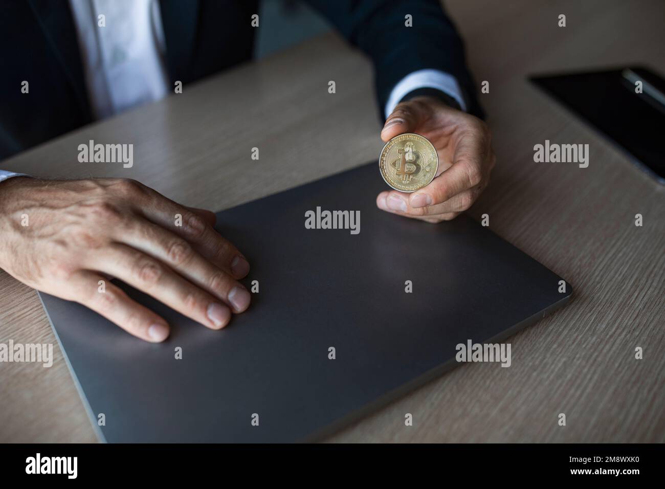 Homme d'affaires en costume tenant le bitcoin dans sa main, assis au travail dans l'intérieur du bureau, court Banque D'Images