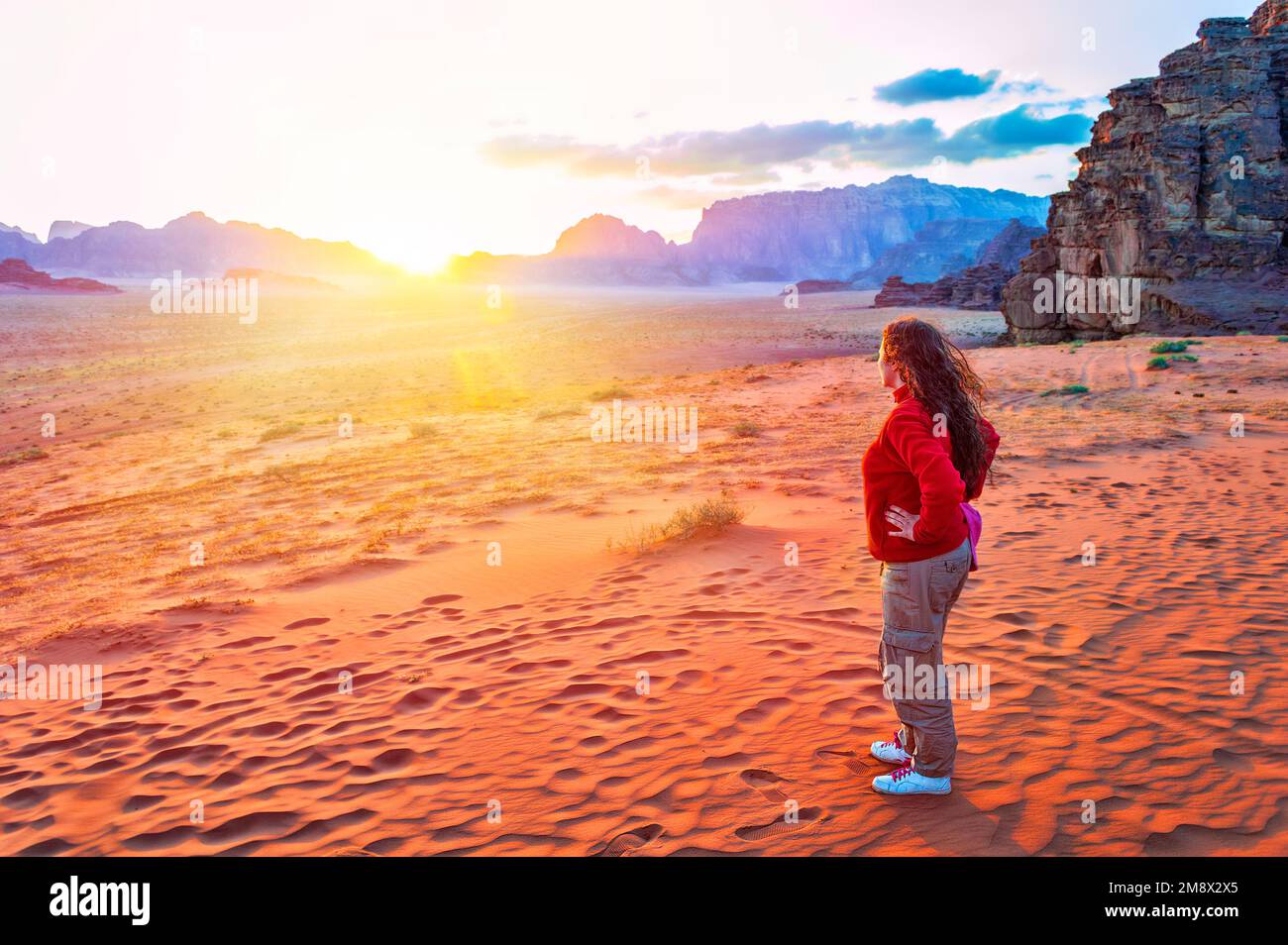 Vue arrière d'une jeune femme explorer dans une veste rouge restant au-dessus d'une dune en profitant d'une vue sur le pittoresque désert rouge en Jordanie Banque D'Images