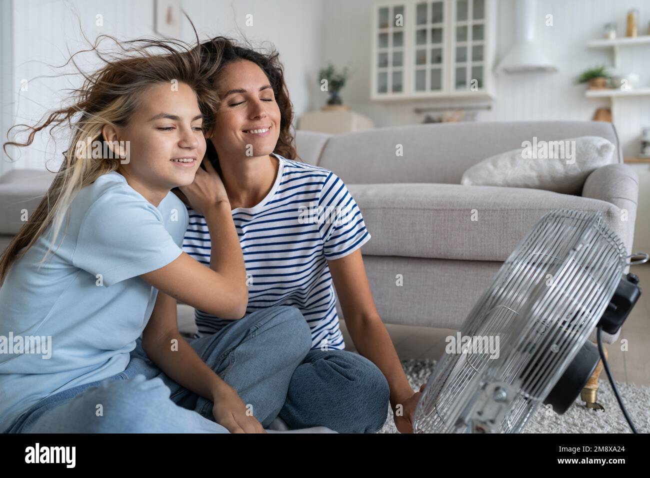 La mère et la fille décontractées et optimistes aiment le vent provenant du ventilateur se trouve au sol dans le salon Banque D'Images
