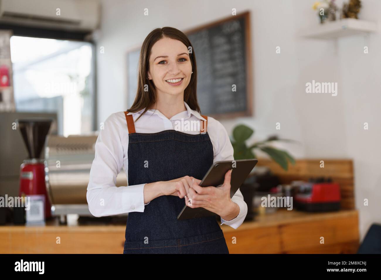 Jeune femme directrice au restaurant avec tablette. Femme propriétaire de café avec enseigne ouverte. Concept de petite entreprise Banque D'Images