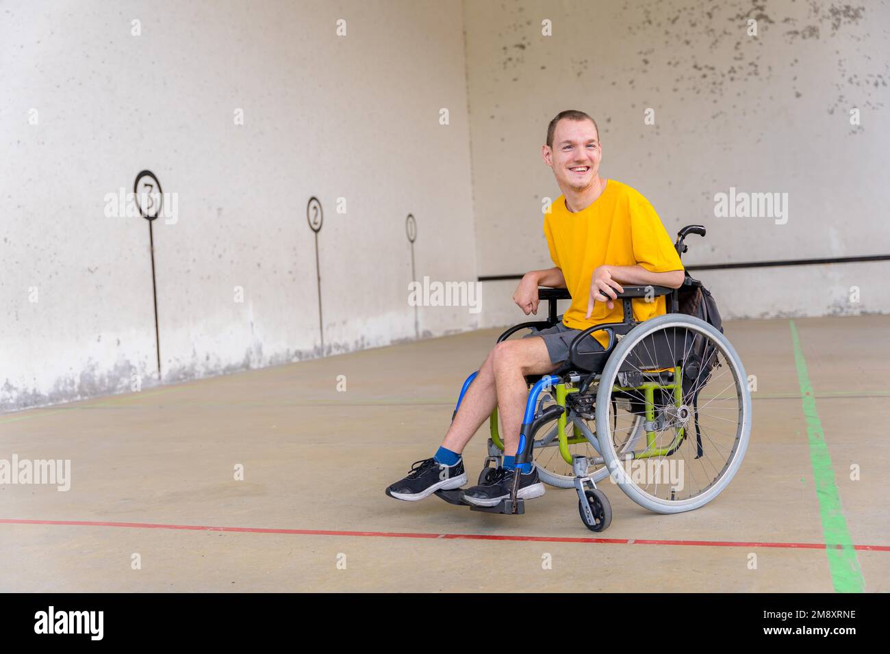 Une personne handicapée dans un fauteuil roulant à une fronton de jeu de pelota basque souriant Banque D'Images