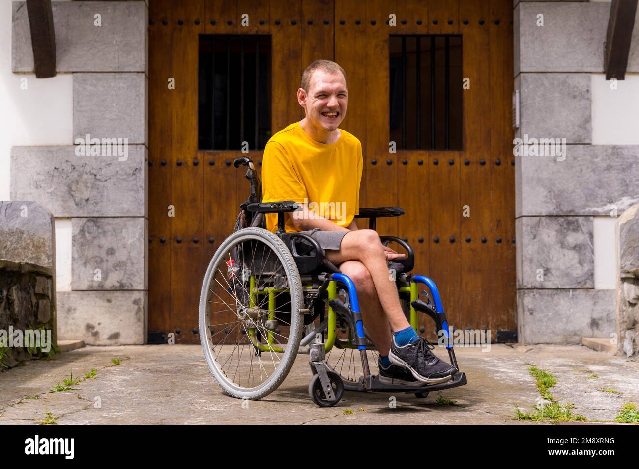 Portrait d'une personne handicapée vêtue en jaune dans un fauteuil roulant à l'entrée de sa maison en souriant Banque D'Images