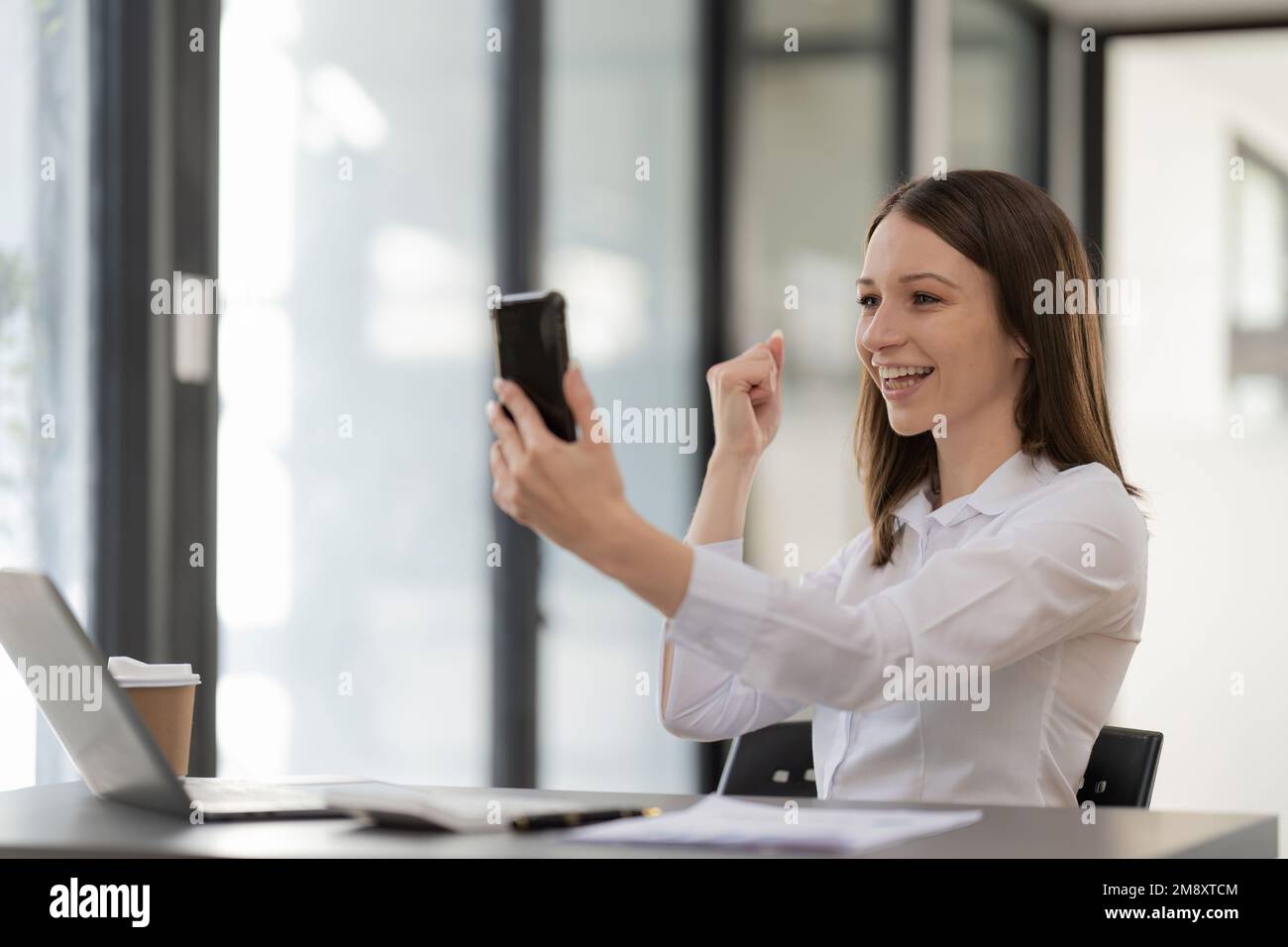 Une femme d'affaires émotive heureuse célèbre la victoire. regarder son téléphone mobile pour une réunion en ligne par appel vidéo au bureau Banque D'Images