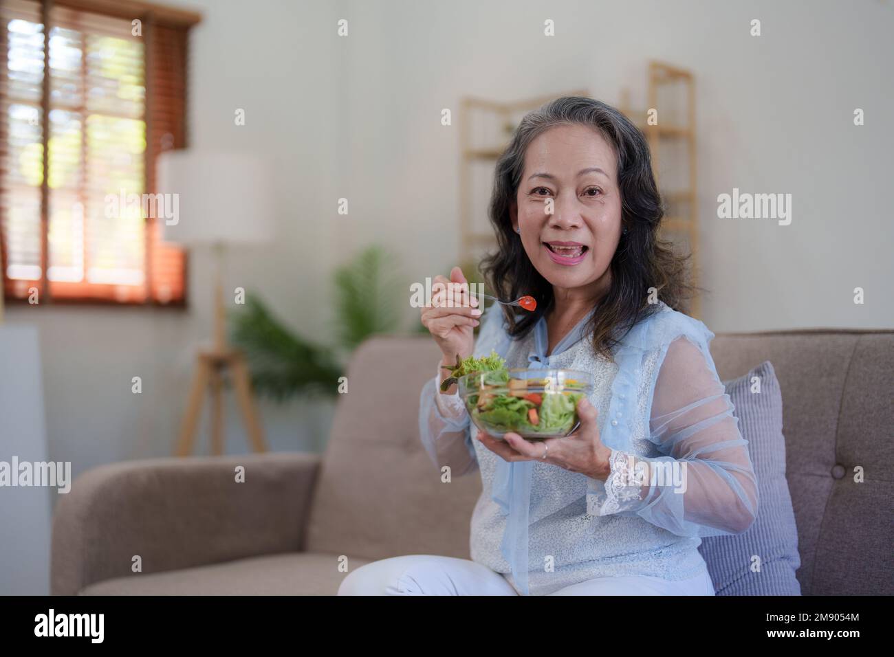 Bonne vieille femme asiatique mangeant de la salade verte fraîche. Femme âgée bonne santé à la maison. Exercice et régime sain concept Banque D'Images