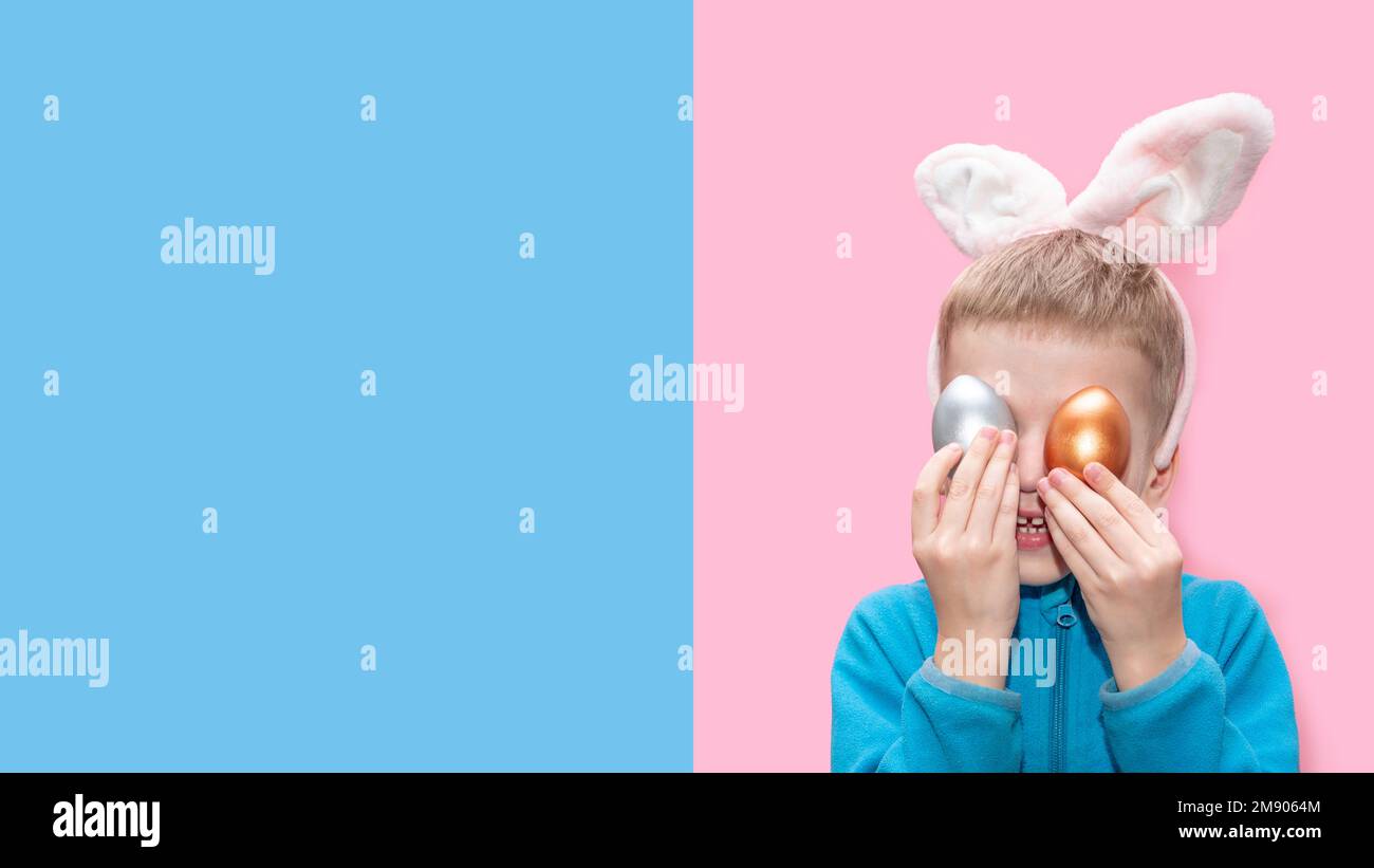 Un petit garçon gai dans une veste bleue et avec des oreilles de lapin tient des oeufs de Pâques colorés sur un fond bleu-rose, bannière, espace de copie. Œuf de lapin de Pâques Banque D'Images