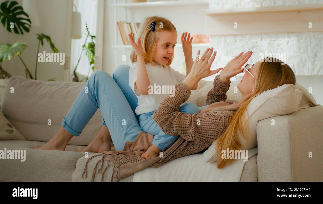 Heureux parent mère de race blanche avec mignon enfant fille enfant fille bébé jouer patty jeu de gâteau à la maison claquant les mains couchant sur canapé canapé à la maison Banque D'Images