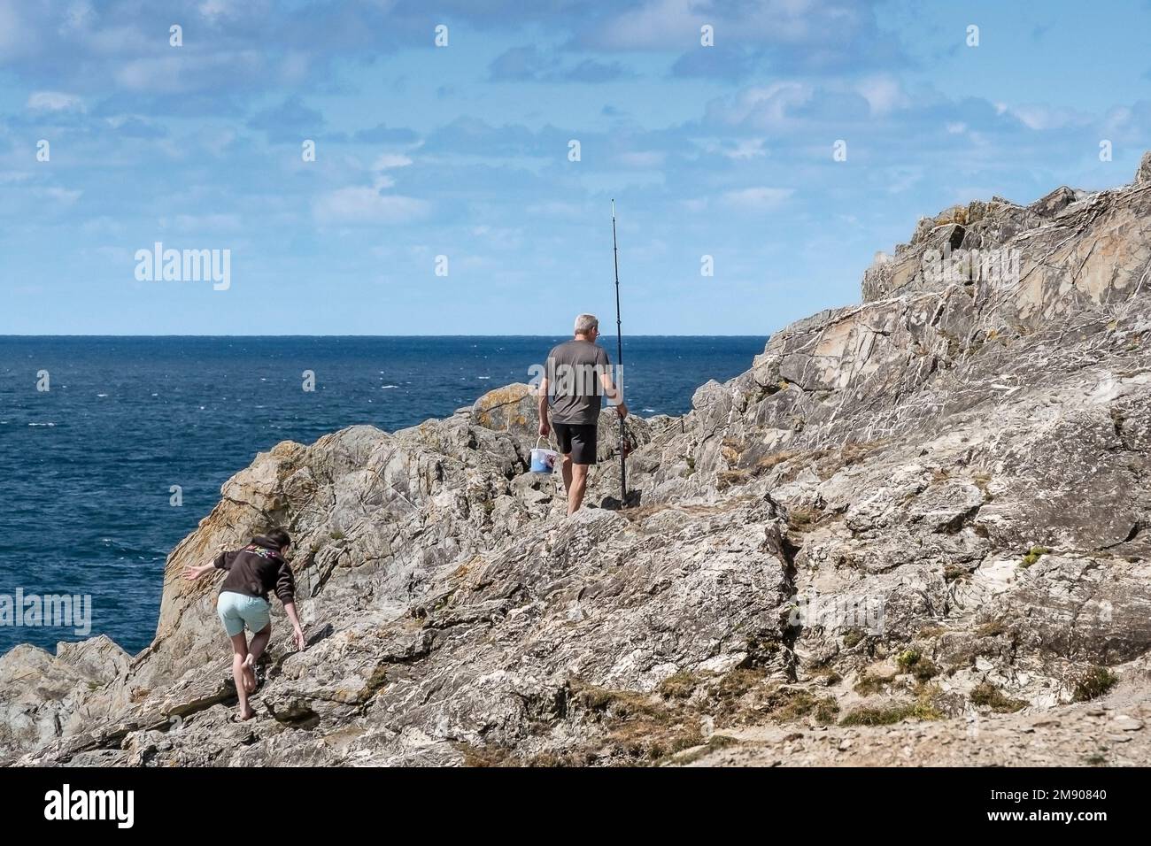 Un père et un fils en vacances marchant sur des rochers pour aller pêcher sur Pentire point East à Newquay, en Cornouailles, au Royaume-Uni. Banque D'Images