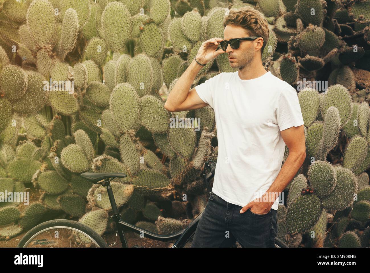 Blonde hipster modèle masculin portant des lunettes de soleil posant près  d'un grand cactus à côté de son vélo Photo Stock - Alamy