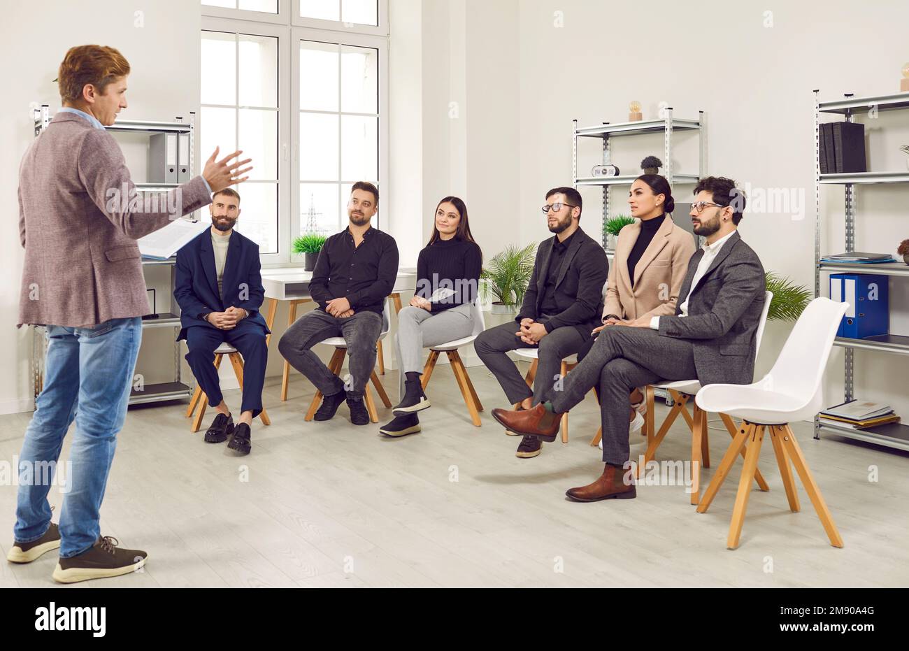 Un coach d'affaires parle à une équipe de jeunes assis sur des chaises dans le bureau de l'entreprise Banque D'Images