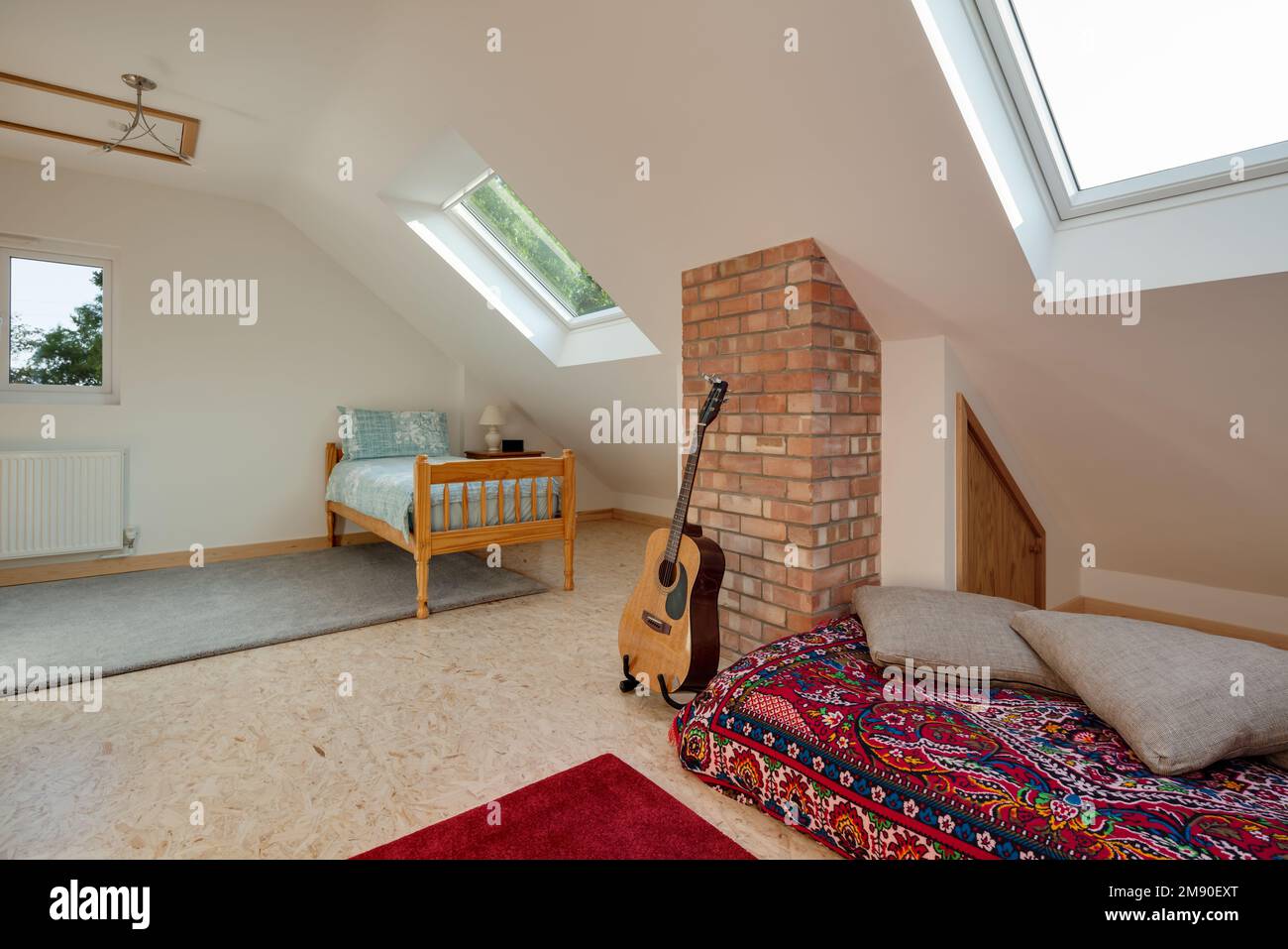 Chambre mansardée meublée avec plafond en pente, lit simple en pin et guitare. Banque D'Images