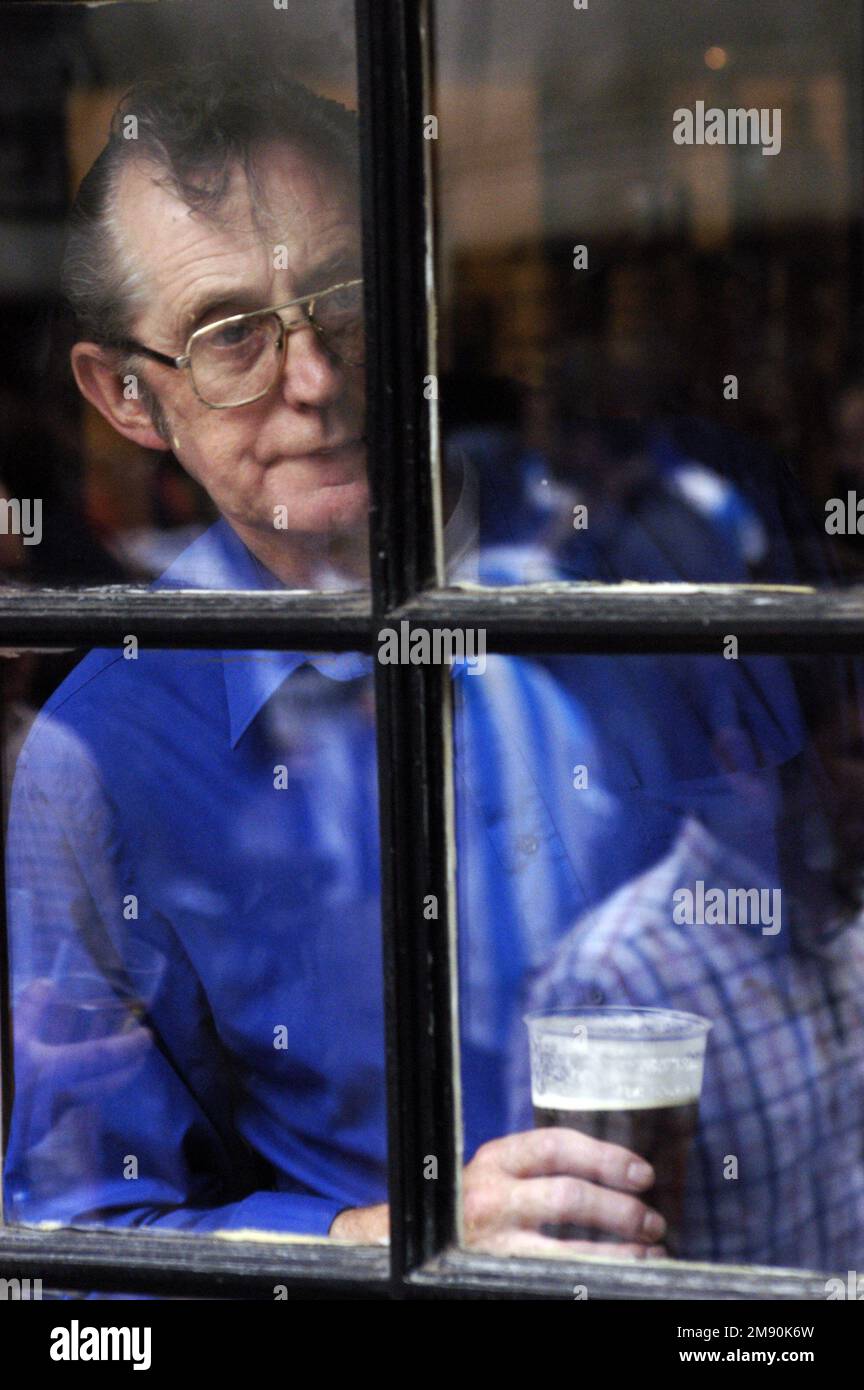 Un vieil homme regarde par la fenêtre d'un pub de la ville tout en tenant une pinte, Cardiff, 2005. Photo : ROB WATKINS Banque D'Images