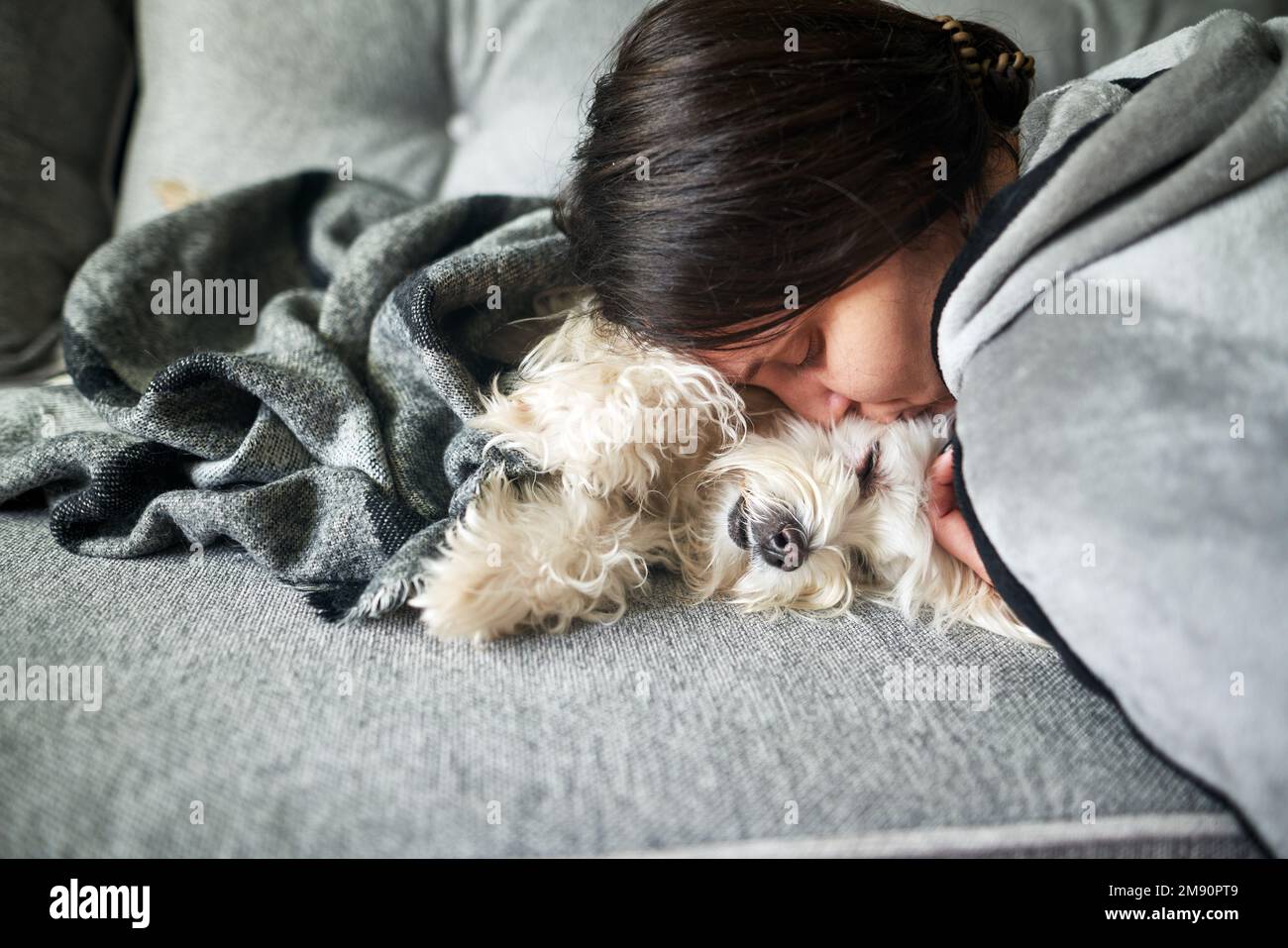 Une jeune femme se câlin et embrasse son chien en étant allongé sur un canapé à la maison. L'amour des animaux, meilleur ami, concept d'animal de compagnie Banque D'Images