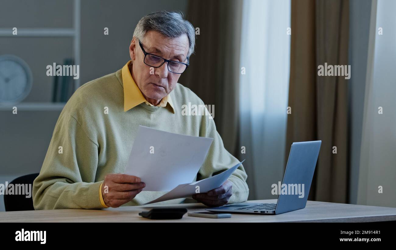 Inquiet perplexe vieux caucasien gris-homme d'affaires 70s homme triste assis à table avec des problèmes de paperasserie avec des documents erreur budget de financement Banque D'Images