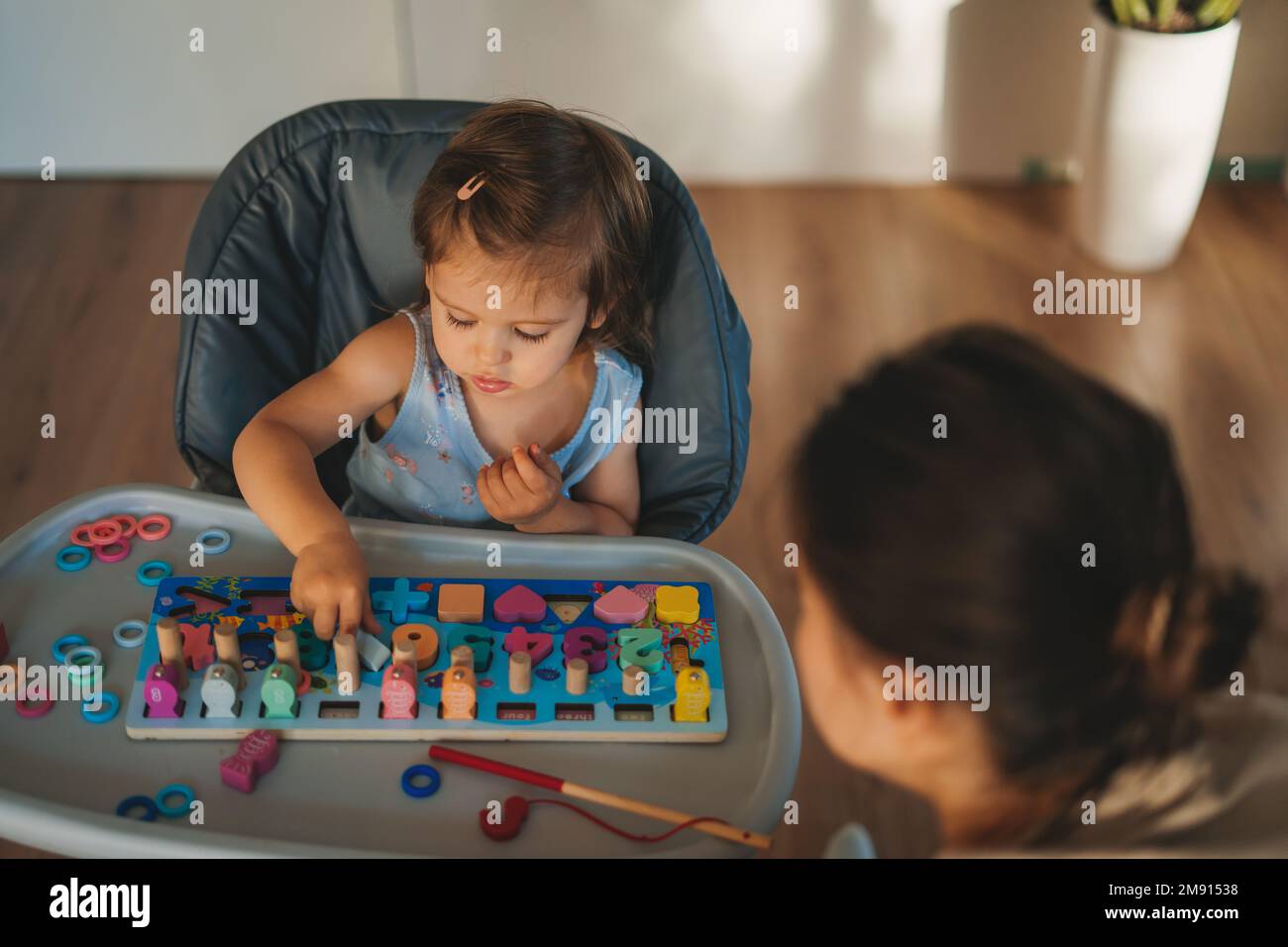 Bébé heureux assis sur une chaise haute et jouant avec des jouets en bois dans une maison moderne et lumineuse. Bébé mignon jouant avec des jouets. Banque D'Images