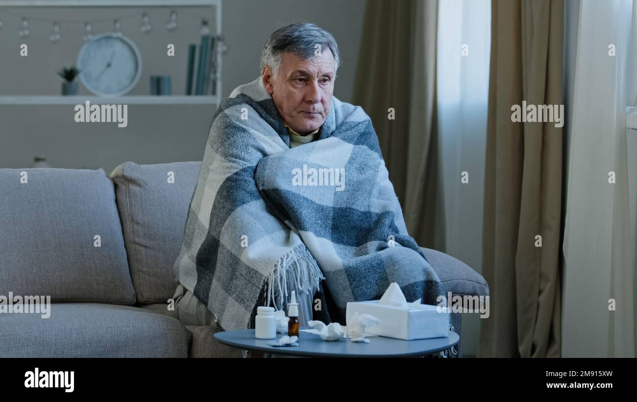Un grand-père âgé de race blanche malade s'assoit couvert d'une couverture sur le canapé à la maison avec un remède au froid un homme adulte âgé malsain ayant des symptômes signes de grippe Banque D'Images