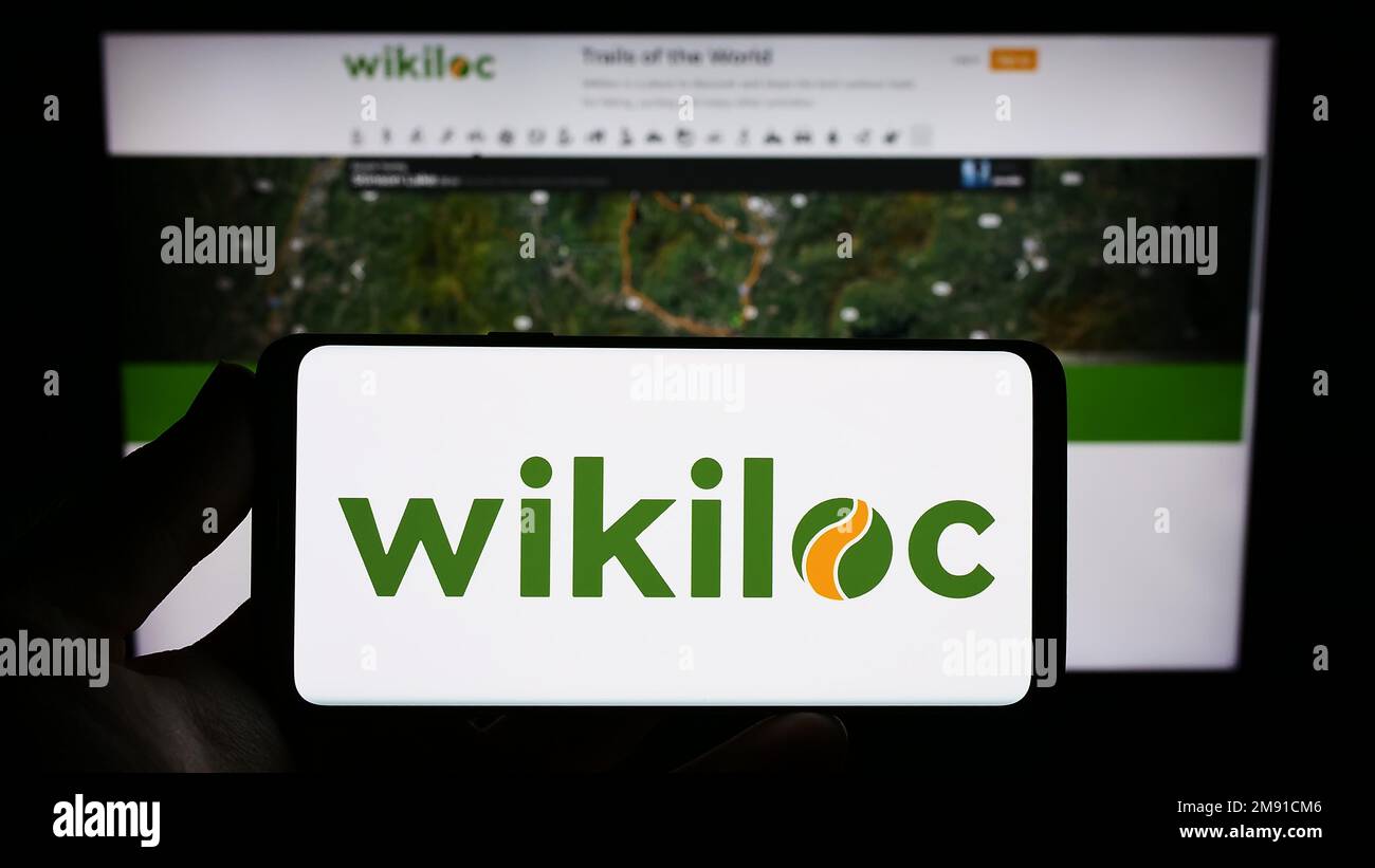 Personne tenant un smartphone avec le logo de la compagnie de sentier GPS Wikiloc Outdoor S.L. à l'écran devant le site Web. Mise au point sur l'affichage du téléphone. Banque D'Images