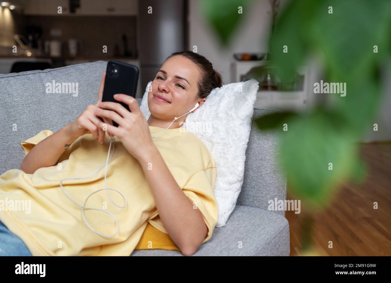 Femme couchée sur un canapé dans le salon et utilisant son téléphone portable style de vie domestique. Banque D'Images