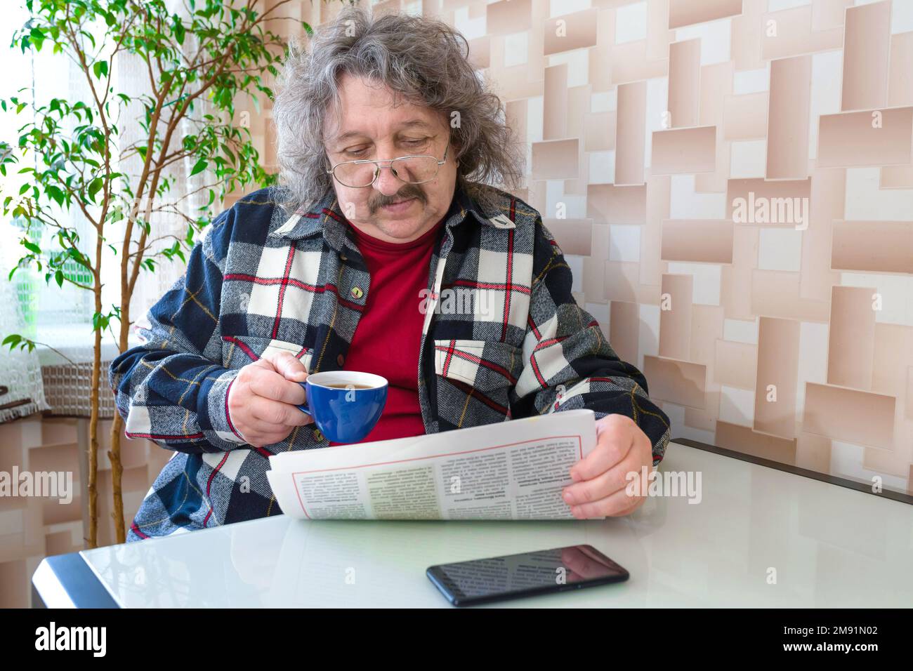 Un portrait d'un pensionné avec une tasse de café et un journal dans ses mains un pensionné lit un journal au sens du vieillissement Banque D'Images