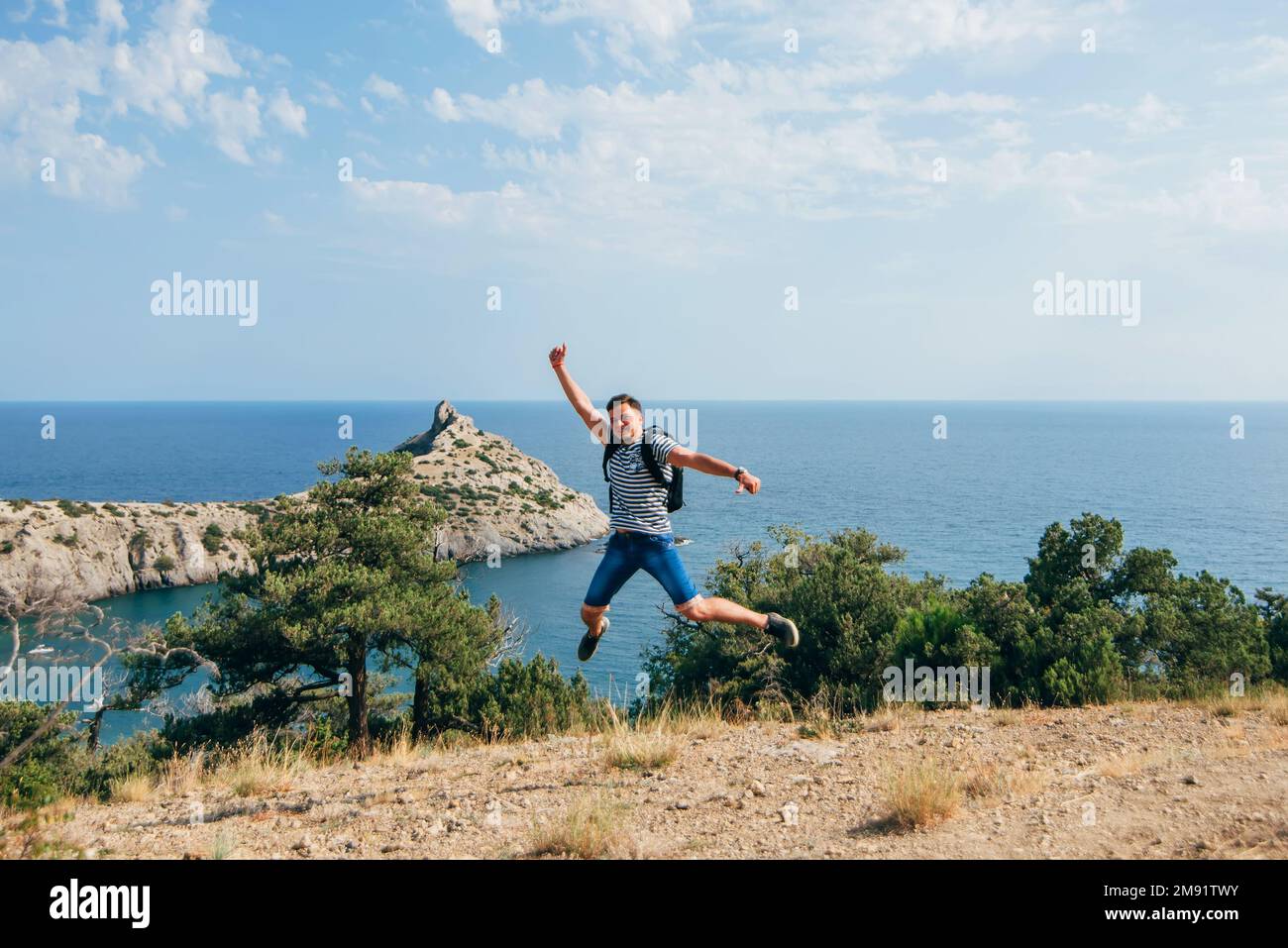 le voyageur masculin saute joyeusement et heureusement dans la nature pendant les vacances d'été dans les montagnes au bord de la mer, symbolisant la liberté Banque D'Images