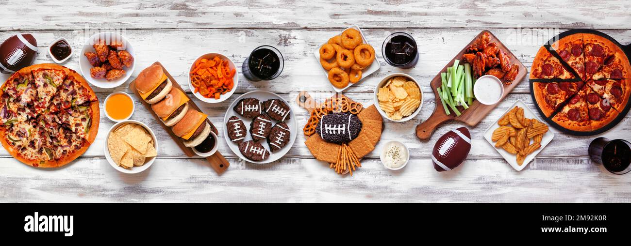 Scène de table de nourriture sur le thème du Super Bowl ou du football. Pizza, hamburgers, ailes, encas et accompagnements. Vue de haut en bas sur fond de bois blanc. Banque D'Images