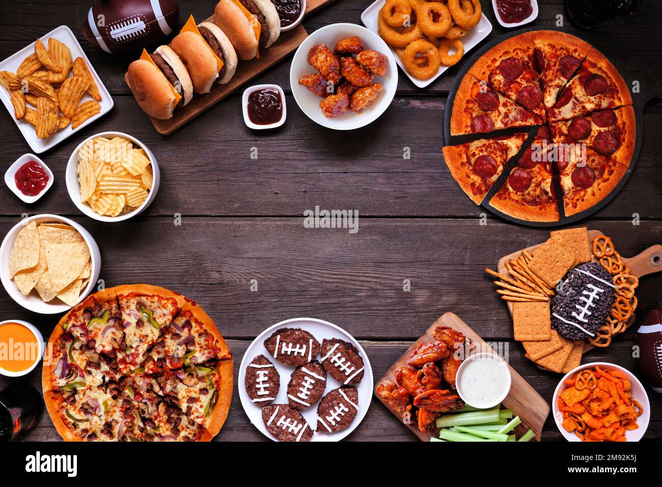 Cadre à nourriture Super Bowl ou football. Pizza, hamburgers, ailes, encas et accompagnements. Vue ci-dessus sur un fond en bois sombre. Banque D'Images