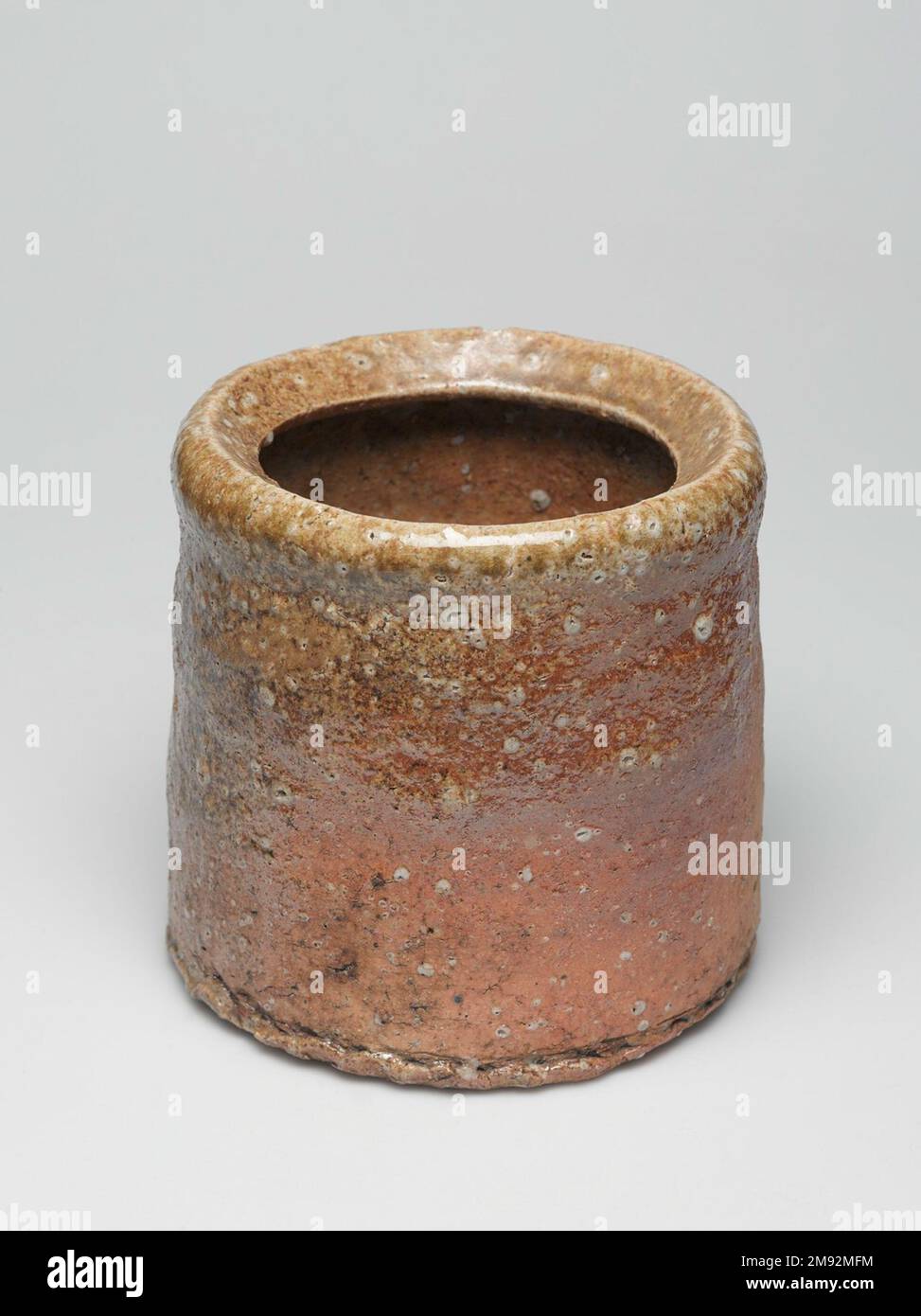 Shigaraki Ware Mizushi (pot d'eau douce pour la cérémonie du thé) Shigaraki Ware Mizushi (pot d'eau douce pour la cérémonie du thé), ca. 1620. Grès cérame avec glaçure de frêne, couvercle laqué ; vaisselle Shigaraki, 6 x 6 1/2 po. (15,2 x 16,5 cm). Alors que la plupart des potiers prennent soin de filtrer les roches de leur argile, les potiers de la région de Shigaraki comprennent que la texture créée par des morceaux rocheux de quartz et de feldspath ajoute un intérêt tactile et visuel à leurs marchandises. Les artisans ajoutent seulement un peu de glaçure, laissant la surface conserver sa granulation. Shigaraki, à l'est de Kyōto, a été un site de four pendant des siècles, à l'origine de la fabrication Banque D'Images