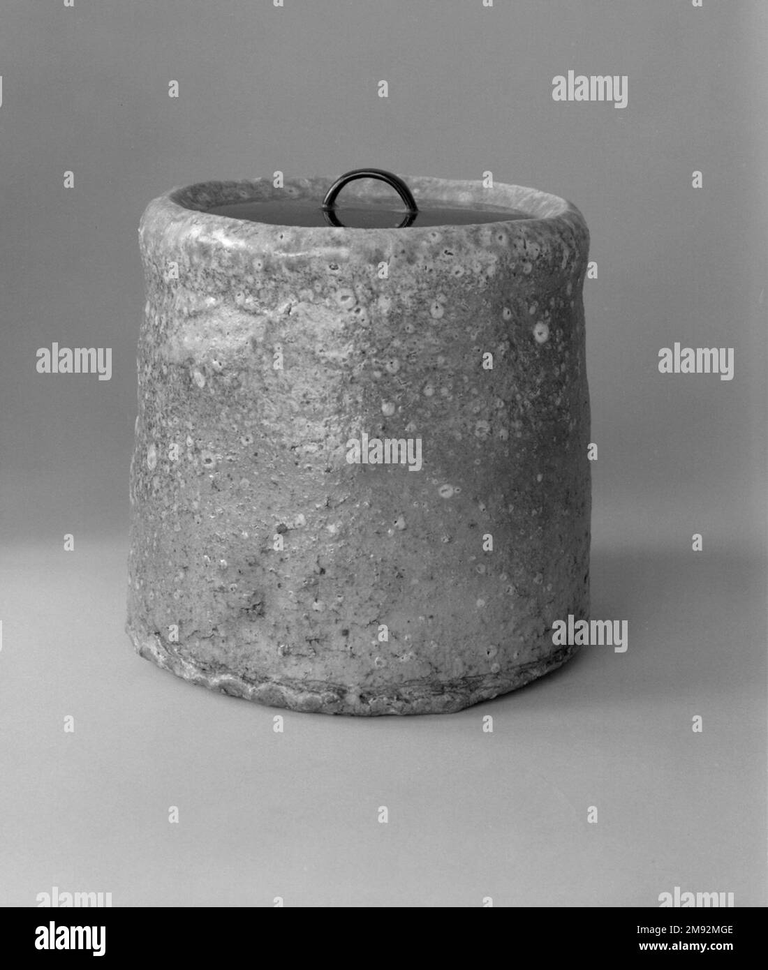 Shigaraki Ware Mizushi (pot d'eau douce pour la cérémonie du thé) Shigaraki Ware Mizushi (pot d'eau douce pour la cérémonie du thé), ca. 1620. Grès cérame avec glaçure de frêne, couvercle laqué ; vaisselle Shigaraki, 6 x 6 1/2 po. (15,2 x 16,5 cm). Alors que la plupart des potiers prennent soin de filtrer les roches de leur argile, les potiers de la région de Shigaraki comprennent que la texture créée par des morceaux rocheux de quartz et de feldspath ajoute un intérêt tactile et visuel à leurs marchandises. Les artisans ajoutent seulement un peu de glaçure, laissant la surface conserver sa granulation. Shigaraki, à l'est de Kyōto, a été un site de four pendant des siècles, à l'origine de la fabrication Banque D'Images