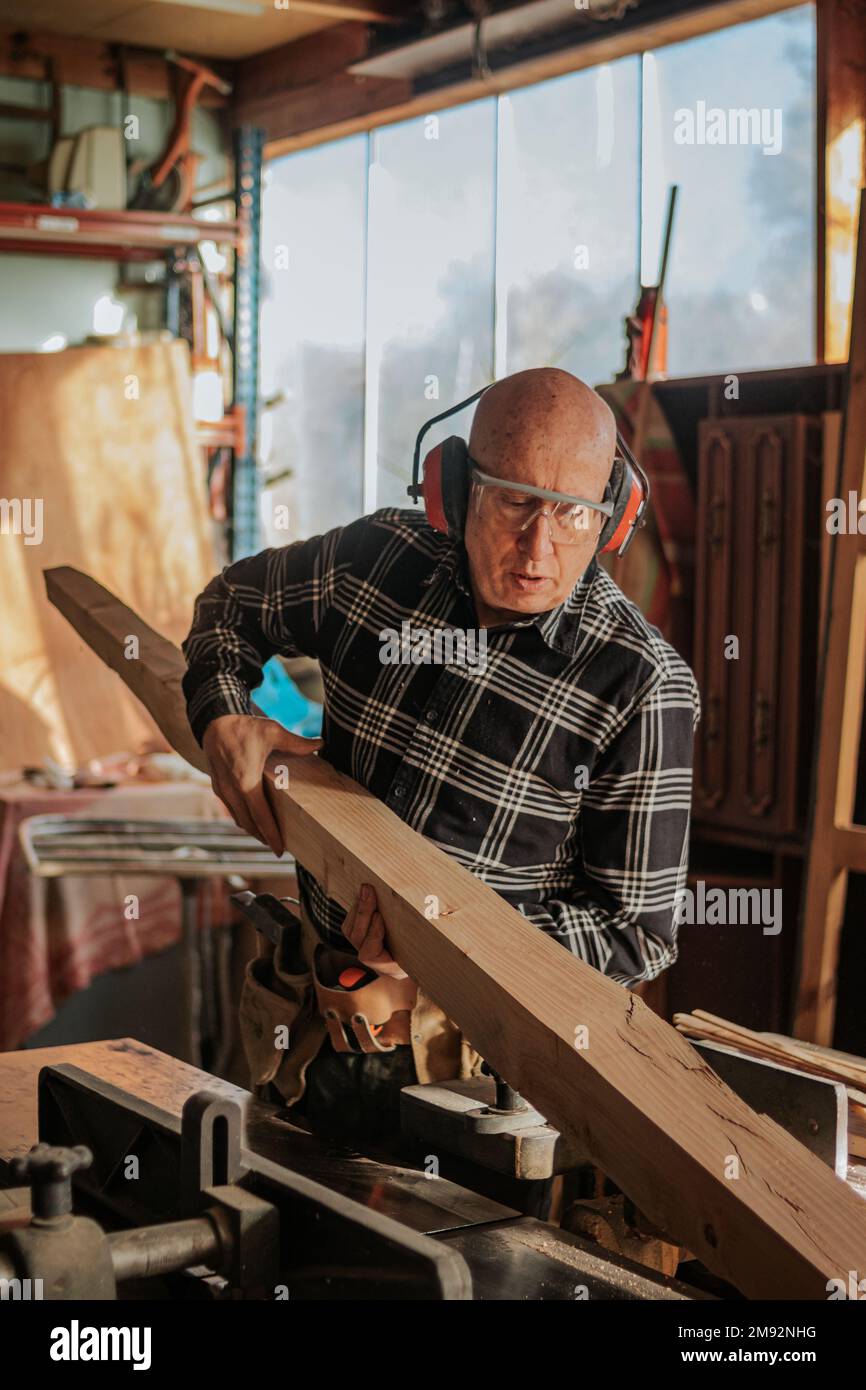 Menuisier mâle dans des lunettes de protection transportant le bois dans la menuiserie professionnelle pendant le processus de réparation Banque D'Images