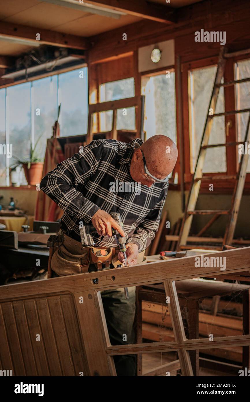 Ouvrier du bois âgé dans des lunettes de protection, en train de percer des planches de bois tout en travaillant dans la menuiserie Banque D'Images