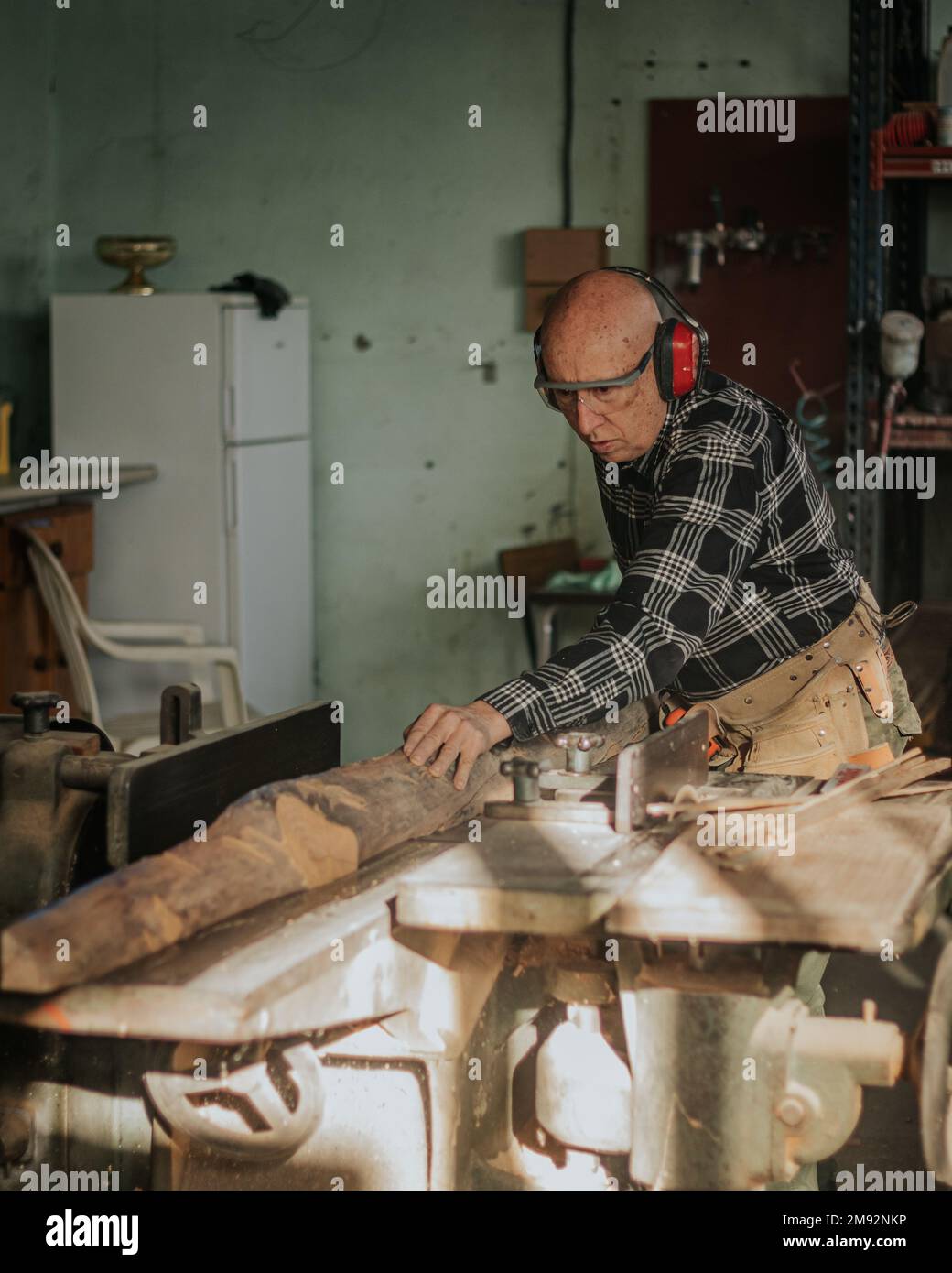 Menuisier mâle mature concentré dans des lunettes de protection coupant pièce en bois tout en créant le motif en bois fait à la main Banque D'Images