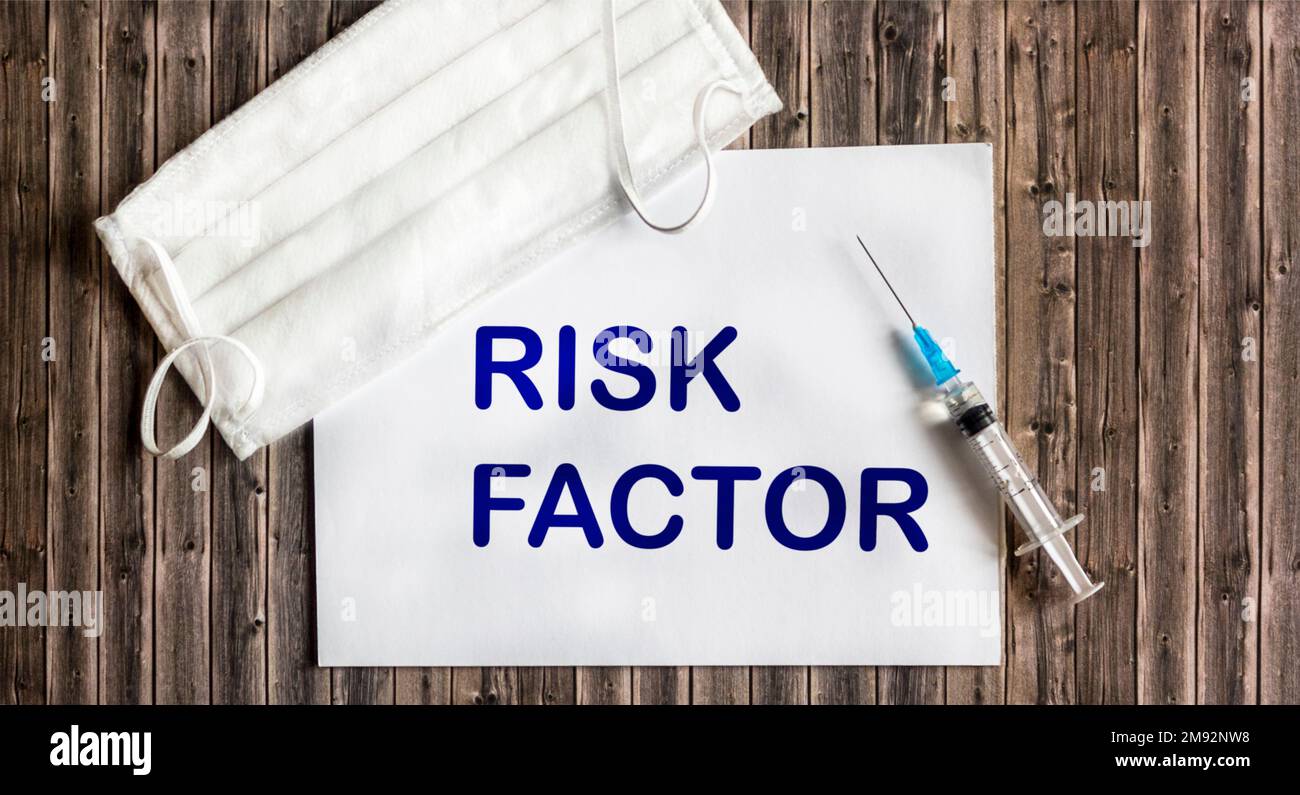 Sur un fond en bois, une seringue, un masque médical et une feuille de papier avec le facteur DE RISQUE de texte à l'intérieur. Vue de dessus. concept médical Banque D'Images