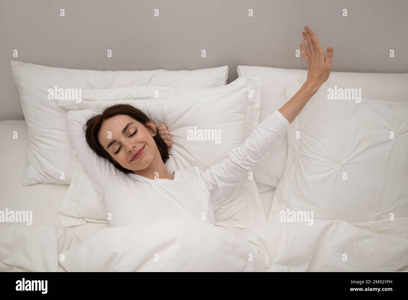 Une jeune femme joyeuse s'étirant dans le lit après s'être réveillée Banque D'Images