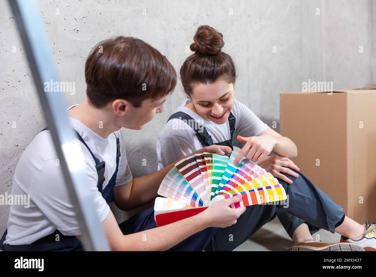 Décoration maison bricolage rénovation concept. Heureux couple assis sur le sol dans la chambre vide de nouveau design de planification de maison. Mari et femme tenant une palette de nuances choisir des couleurs pour peindre le mur dans une nouvelle maison Banque D'Images