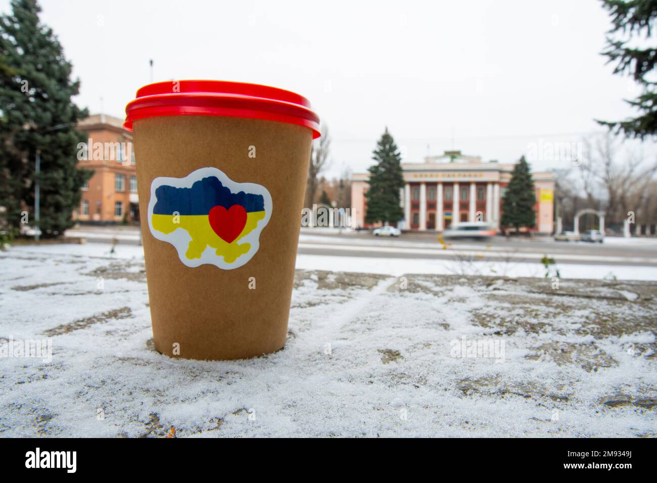 Hiver. Temps froid. Une tasse de café avec un autocollant patriotique « J'aime l'Ukraine » sur le sol, sur fond d'une rue de la ville (gros plan) Banque D'Images