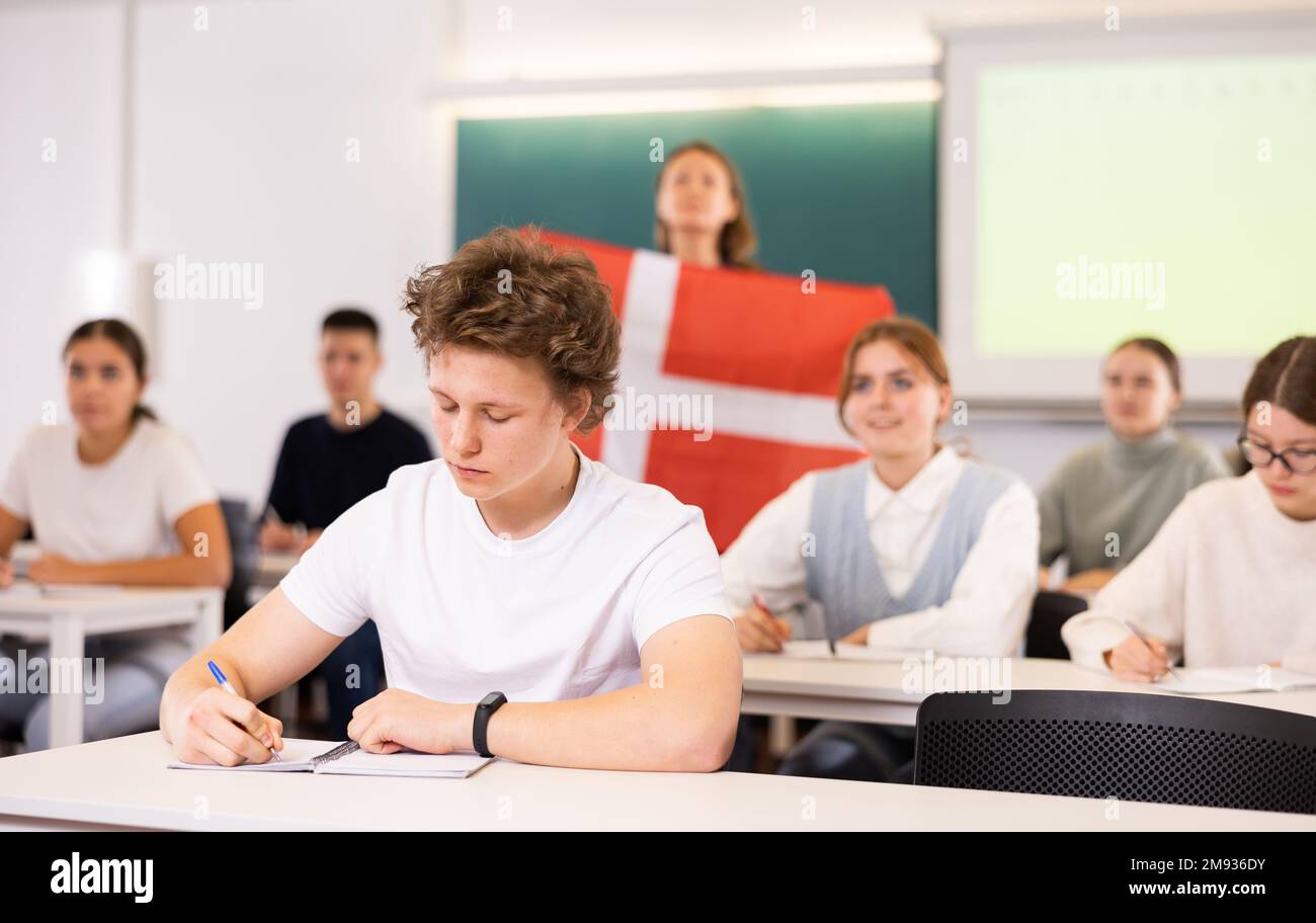 Un enseignant du secondaire parle aux élèves du Danemark et détient un drapeau du Danemark entre les mains. Banque D'Images