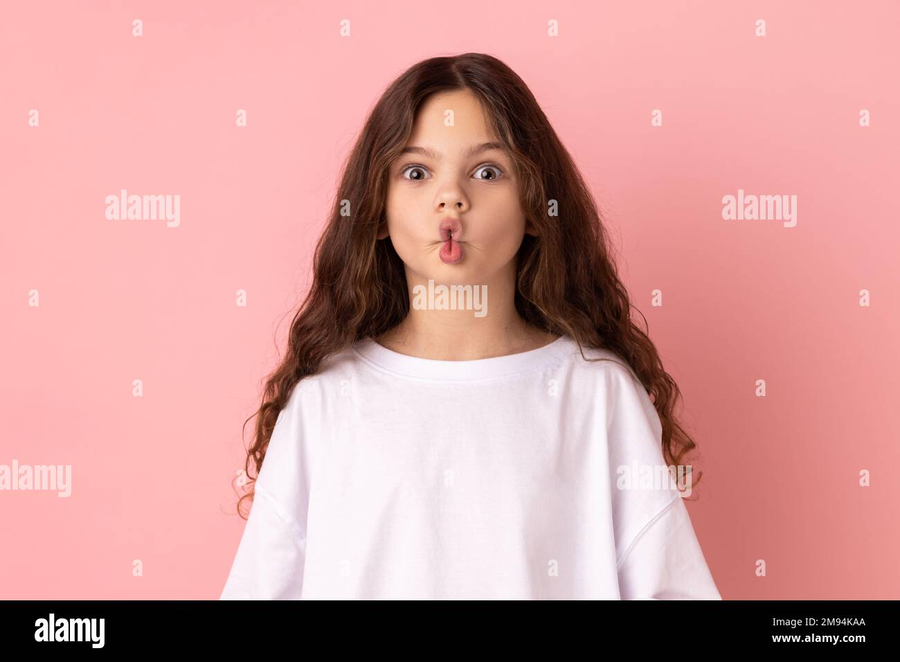 Portrait de la petite fille drôle excitée de faire le visage de poisson avec les lèvres et les grands yeux émerveillés, regardant surpris et stupide à l'appareil-photo, s'est demandé expression. Studio d'intérieur isolé sur fond rose. Banque D'Images