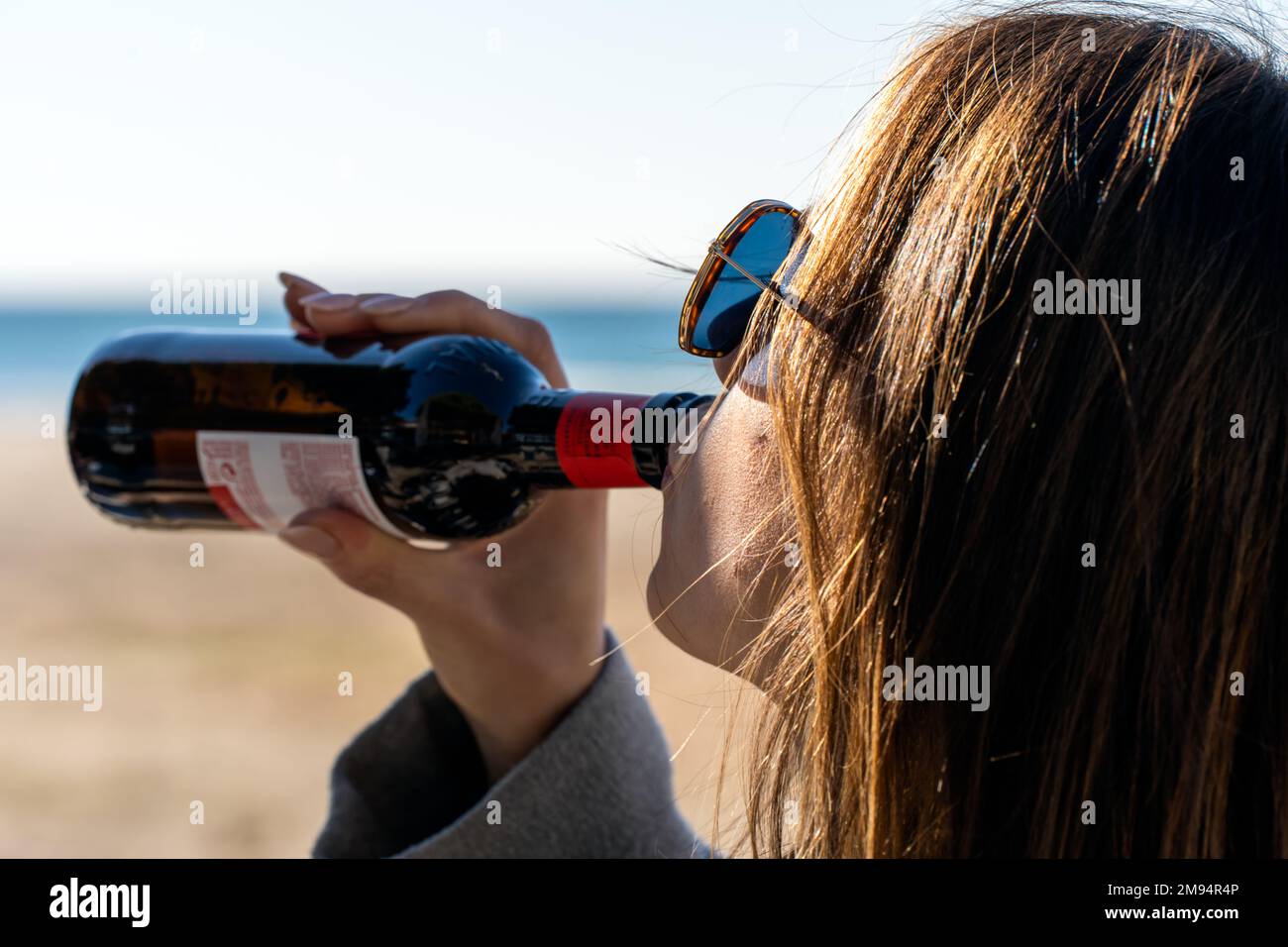 Vue latérale de la petite fille en lunettes de soleil buvant de la bière froide à partir d'une bouteille de verre tout en passant du temps sur la mer Banque D'Images