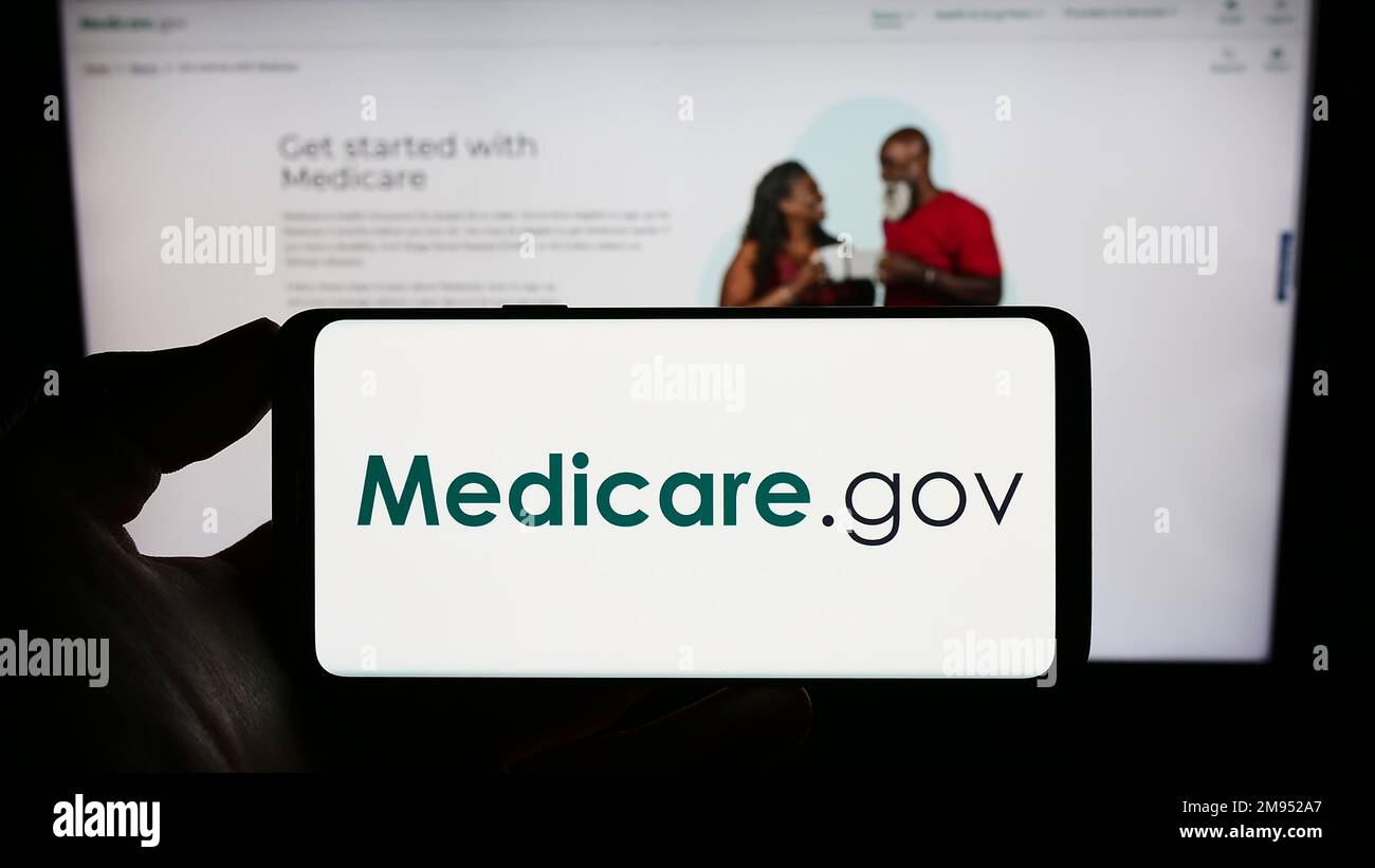 Personne tenant le téléphone cellulaire avec le logo du programme d'assurance maladie américain Medicare à l'écran en face de la page Web. Mise au point sur l'affichage du téléphone. Banque D'Images