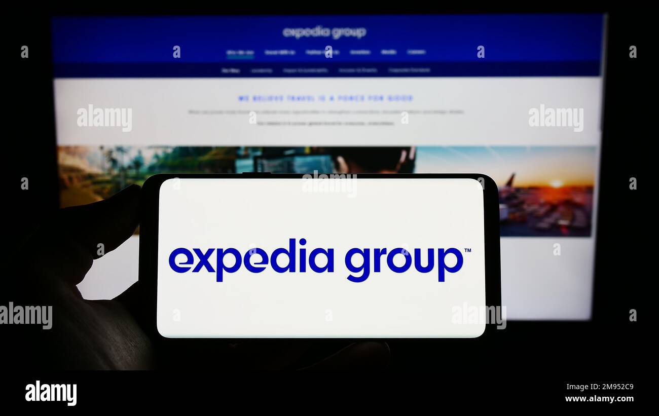 Personne tenant un téléphone portable avec le logo de la compagnie de voyage en ligne américaine Expedia Group Inc. À l'écran en face de la page Web d'affaires. Mise au point sur l'affichage du téléphone. Banque D'Images