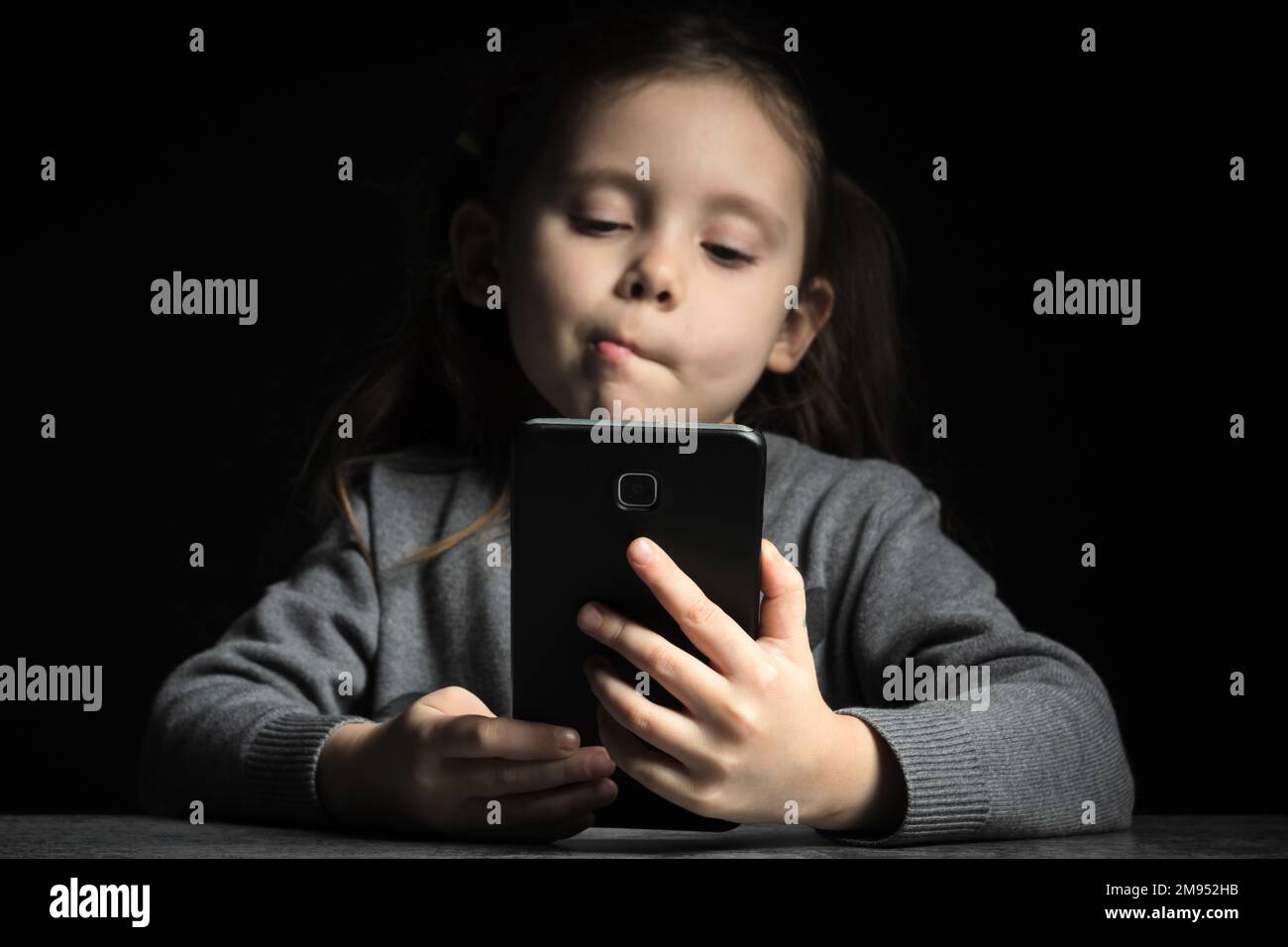 Petite fille avec un visage réfléchi la nuit communique sur Internet. Dépendance et insomnie de gadget d'enfant, problèmes psychologiques Banque D'Images