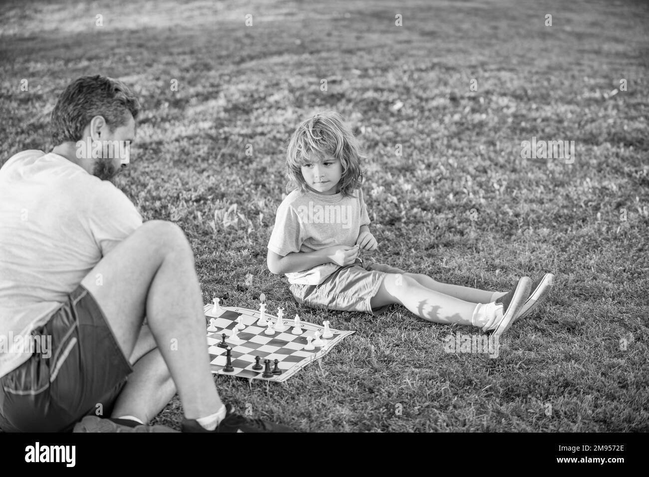 bonne famille de parents et fils garçon jouant aux échecs sur l'herbe verte dans le parc extérieur, échecs Banque D'Images