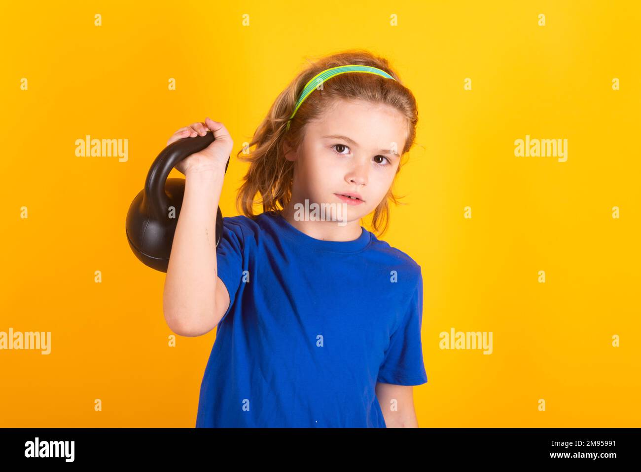 Enfants sportifs, portrait isolé en studio sur fond jaune. Enfant garçon pompant les muscles du biceps avec la kettlebell. Fitness avec haltères pour les enfants. Banque D'Images
