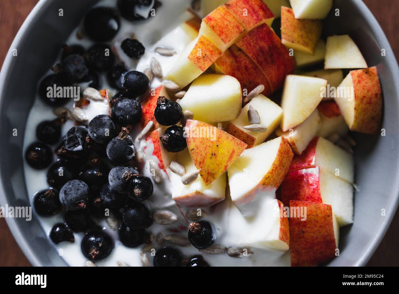 Bol à petit-déjeuner sain à base de fruits et de yaourt sur une surface en bois avec des tranches de pomme, de cassis et de graines de tournesol. Vue de dessus, gros plan. Banque D'Images