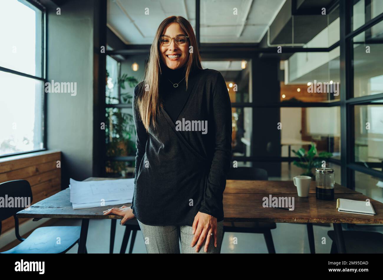 Femme entrepreneur réussie souriant à la caméra tout en se tenant dans un bureau. Bonne jeune femme d'affaires debout dans la salle de réunion d'un travail moderne Banque D'Images
