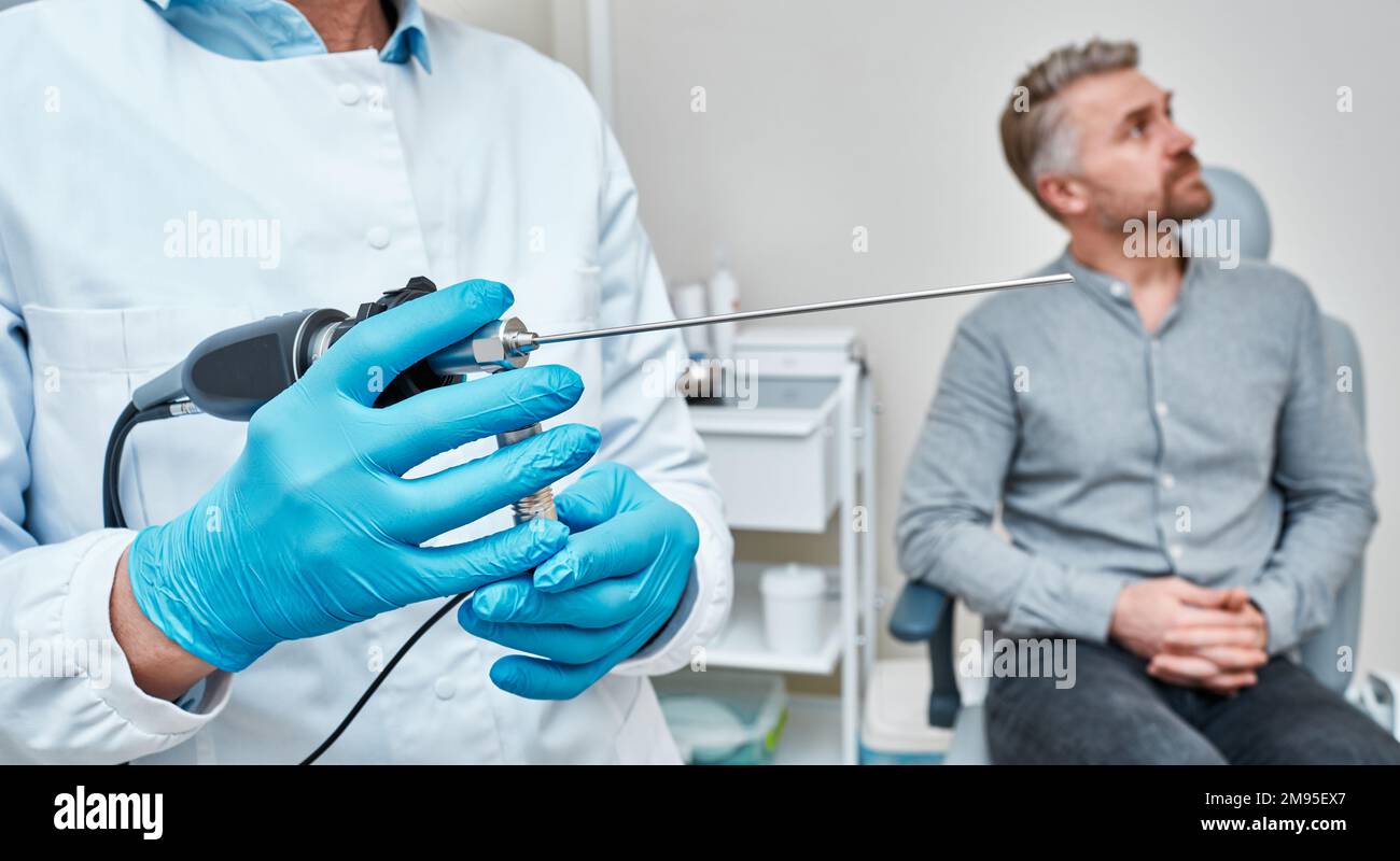 Médecin oto-rhino-laryngologiste tenant un vidéo-endoscope pour le contrôle endoscopique des organes ORL avant la procédure d'examen d'un homme adulte assis dans un fauteuil ORL Banque D'Images